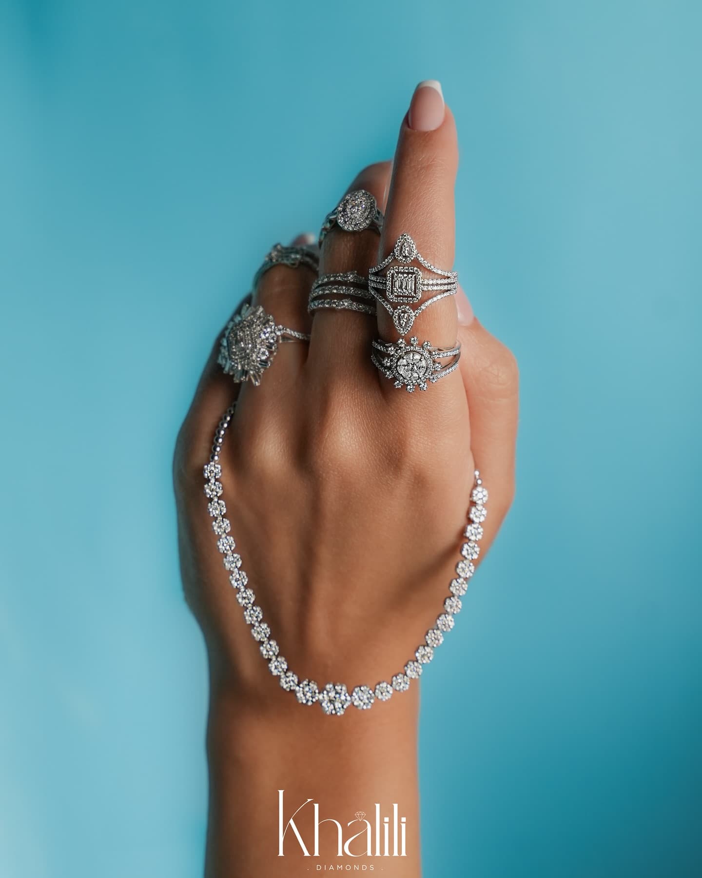 A hand adorned with multiple Khalili diamond rings and a diamond tennis necklace